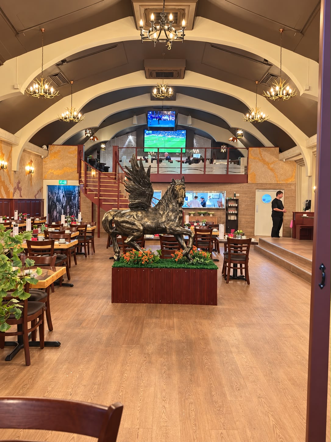 The vaulted dining room at Tavern Co. Social, with chandeliers, a bronze winged horse and sport on the screens